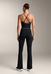 Top sportiv negru, scurt, cu bretele încrucișate pe spate, asortat cu pantaloni leggings negri cu croială evazată. Textură netedă, branding minim vizibil.