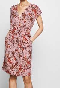 Kukkakuvioinen mekko pehmeässä vaaleanpunaisessa sävyssä, jossa on punaisia ja ruskeita kuvioita. V-pääntie, lyhyet hihat, joustava vyötärö ja sivutaskut. Kevyt kangas.