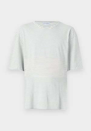 Jonge man staand met een gestreept grijs T-shirt, beige short met touwriem, witte sokken en witte sneakers op een effen lichte achtergrond.