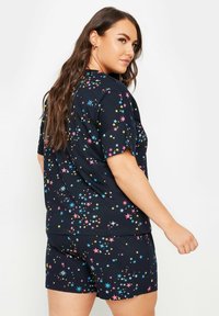 Svart pyjamasset med korta ärmar och stjärnmönster i rosa, blått och gult. Toppdelen har en avslappnad passform; shortsen är också gjorda av mjukt tyg.