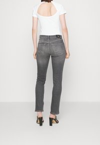 Grå jeans med raka ben, bakfickor och en vit topp med ett stort utskärning på ryggen. Svarta klacksandaler.