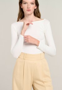 White long-sleeve top with a boat neckline, paired with high-waisted beige pants featuring a pleated design and structured waistband.