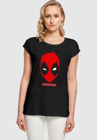 Tricou negru cu un grafic mare al măștii roșii Deadpool, cu ochi albi și textul "DEADPOOL" în roșu îndrăzneț în partea de jos. Mâneci scurte.
