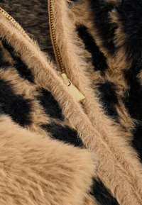 Faux-Fur-Stoff in tan und schwarzem Leopardenmuster, ausgestattet mit einem goldenen Reißverschluss mit einem strukturierten Zug, der die samtige Textur betont.