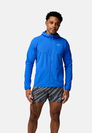 Blue lightweight hooded jacket with a zip front and two pockets, paired with black and gray striped shorts. Smooth texture, athletic fit.
