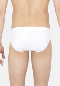Witte katoenen onderbroeken met een effen ontwerp, zachte textuur en een brede elastische tailleband. Zichtbare stiksel langs de randen en minimale bedekking.
