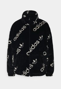 Černá bunda z umělé kožešiny s vysokým límcem, zdobená bílým textovým vzorem a logem po celém povrchu. Zapínání na zip a boční kapsy. Jemná textura.