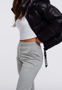 Czarna puchowa kurtka o błyszczącej fakturze z różowymi akcentami, zestawiona z jasnoszarymi dresami. Oba elementy garderoby mają luźny krój.