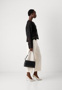 Svart blonde cropped topp med lange ermer, hvite vide bukser, svart håndveske og nude høyhælte sko; minimalistisk design.