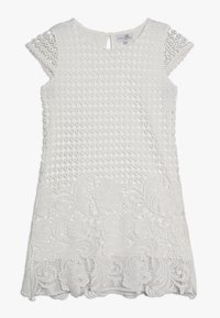 Vit klänning med en texturerad överdel med cirkulära mönster och spetsiga ärmar. Den nedre halvan är detaljerad med intrikat blommönstrad spets.