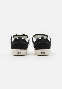 Sorte sued sneakers med hvite detaljer, med en mørk såle og logo på hælen. Rund tå og en løftestrop bak.