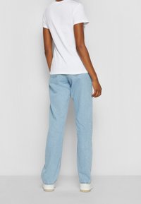 Witte katoenen T-shirt met korte mouwen, gecombineerd met lichtblauwe denim jeans met een relaxte pasvorm en taps toelopende pijpen, gedragen met witte sneakers.