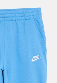 Blå bomullssweatpants med elastisk midjebånd, sidelommer og en hvit Nike-logo på venstre lår. Glatt tekstur, avslappet design.