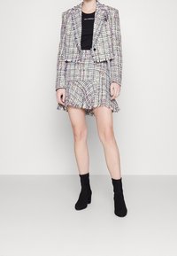 Ensemble deux pièces composé d'un blazer court en tweed multicolore avec un ourlet à franges et d'une jupe assortie. Porté avec des bottines en daim noires.