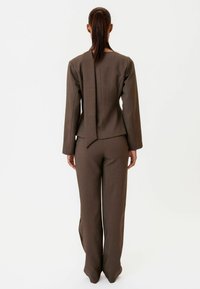 Hnedý prispôsobený oblek s dlhými rukávmi, priliehavým strihom a širokými nohavicami, zdobený detailom stuhy na chrbte a hladkou textúrou.