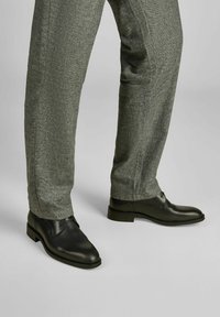 Zwarte leren schoenen met een gladde afwerking, ronde neus, lage hak en subtiele stiknaden, gecombineerd met gestructureerde grijze broek.