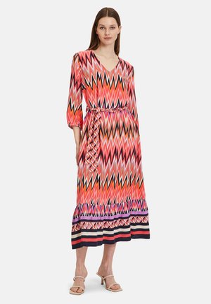 Robe longue à motifs zigzag dans des teintes de rose, orange et noir, avec des manches trois-quarts et une taille ceinturée. Détail à volants au bas.
