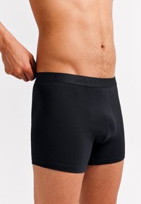 Black boxer briefs with a stretchy waistband featuring subtle branding. Smooth fabric with a fitted design, short legs, and no visible patterns.