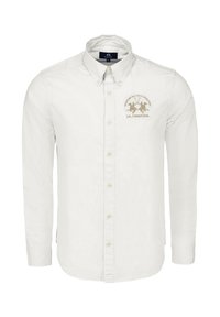 Bílá košile na knoflíky z bavlny. Má špičatý límec, dlouhé rukávy a zlatě vyšívané logo na levé straně hrudi.