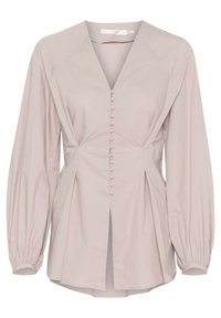 Blouse beige claire à manches longues avec col en V, boutons recouverts de tissu sur le devant, manches froncées et légère fente à l'avant de l'ourlet.