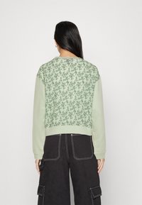 Felpa verde con un motivo floreale sul retro, polsini e orlo a costine; abbinata a pantaloni cargo neri con tasche e cuciture a contrasto.