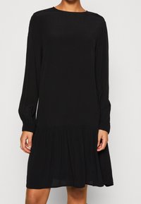Vestido negro de mangas largas hecho de un tejido ligero, con un escote redondo, mangas fruncidas y un dobladillo escalonado y fluido.