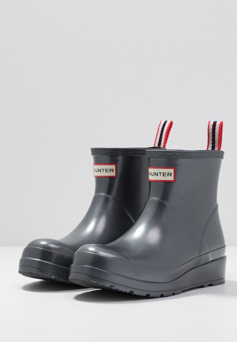Botas de goma gris hasta el tobillo con punta redondeada, que cuentan con una lengüeta de tira roja y negra y una suela texturizada negra sólida.
