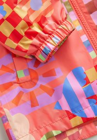 Farbige, leichte, wasserabweisende Jacke mit einem lebhaften abstrakten Muster, das Formen in Pink, Orange und Blau zeigt. Elastische Bündchen.