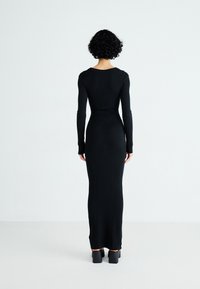 Abito a coste nere con maniche lunghe, silhouette aderente e orlo dritto, abbinato a scarpe con tacco spesso.