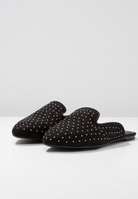 Svarta mockaskor med en slip-on design, prydda med ett mönster av små vita prickar, med platta sulor och rundade tår.