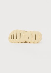 Gul sandal med et segmenteret design, der har udsparinger i sålen. Glat tekstur, let og fleksibel konstruktion.