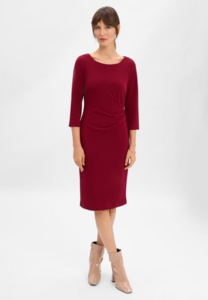 Bordowa sukienka do kolan z rękawami o długości trzech czwarte, z detalem w formie skrętu w talii; zestawiona z beżowymi botkami za kostkę z kwadratowym noskiem.