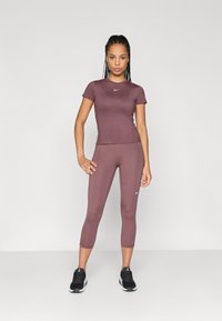 Tettsittende treningsoberstykke og capri-leggings i dempet lilla, laget av elastisk stoff med en jevn tekstur. Har små hvite logo-detajler.