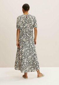 Femme portant un haut à motifs abstraits noir et blanc à manches courtes et une jupe longue assortie, debout pieds nus sur un sol clair.