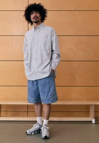 Vaaleansinivalkoraidallinen nappipaita yhdistettynä sinisiin farkkushortseihin, joissa on musta Nike-logo, sekä hopeisiin urheilukenkäpariin.