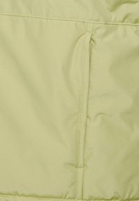 Helle grüne gepolsterte Stoff mit einer subtilen gerippten Textur und gesteppten Details. Verfügt über eine seitliche Tasche, die in das Design integriert ist.