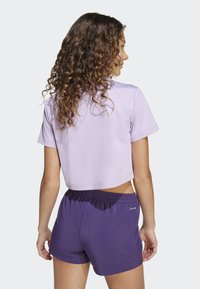 Maglietta cropped lilla abbinata a pantaloni corti viola. Il tessuto sembra leggero e liscio, con una vita elasticizzata sui pantaloni.