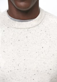 Hellgrauer, gesprenkelter Strickpullover mit geripptem Rundhalsausschnitt. Weiche Textur, die im Stoff kleine dunkle Sprenkel aufweist.