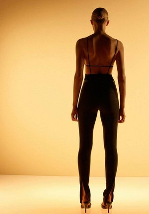 Pantalons noirs ajustés à taille haute avec des fentes accentuées au bas. Fines bretelles réglables au dos. Texture lisse, design élégant.