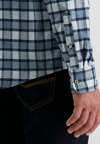Blauw-wit geruit overhemd met een gestructureerde kraag, voorzien van een manchet met knoopdetail, gecombineerd met donkere jeans.