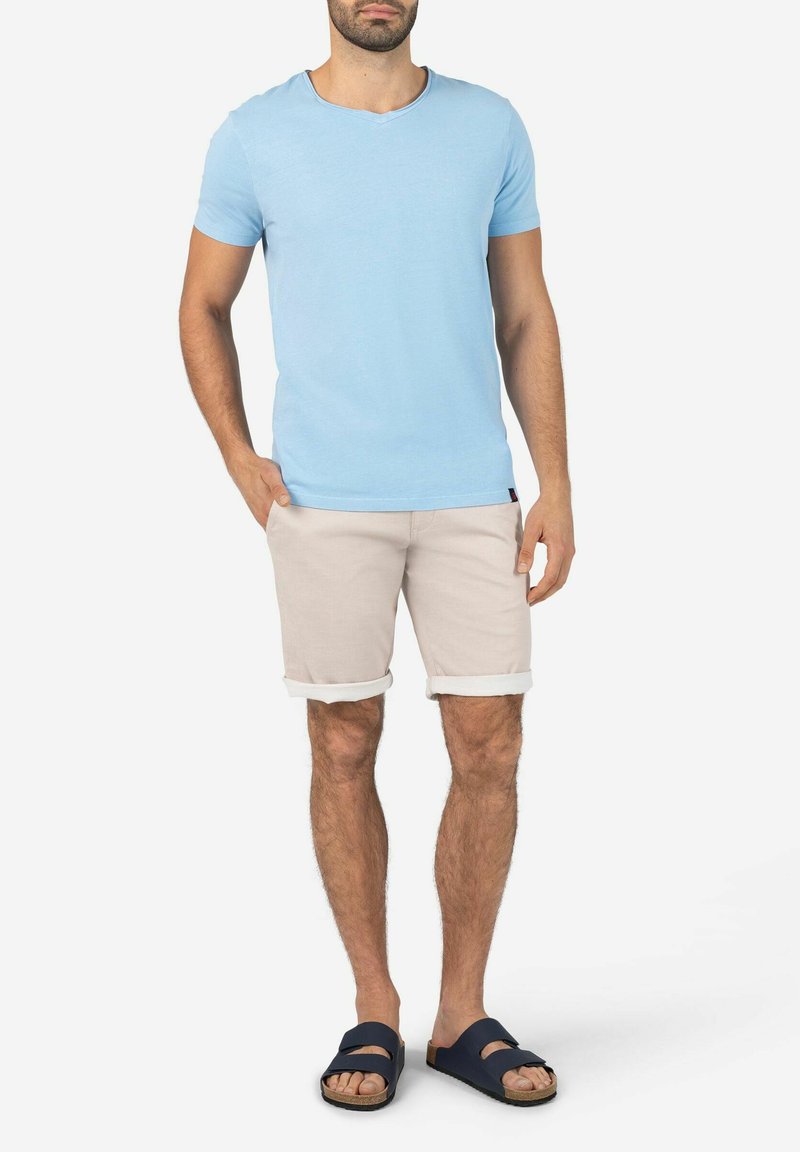 Light blue cotton t-shirt with short sleeves, paired with beige rolled shorts. Sandals feature a navy two-strap design with a flat sole.
