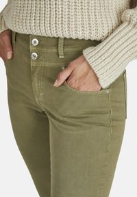 Jeans elásticos verde oliva con un corte ajustado, que cuentan con un cierre de botón y cremallera, bolsillos laterales y una textura suave.