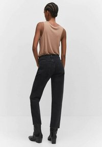 Jeans negros de cintura alta con corte recto, combinados con una blusa sin mangas beige. La ropa tiene una textura suave y sin patrones visibles.
