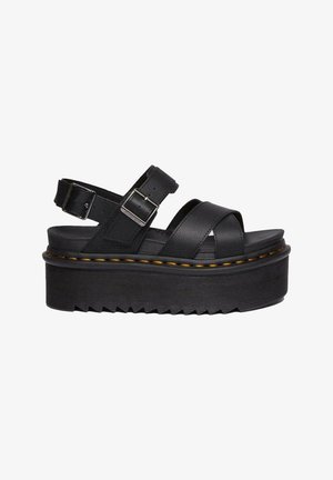 Black platform sandals made of smooth leather, featuring crisscross straps, a buckled ankle strap, and a textured rubber sole with zigzag pattern.