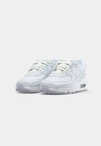 Para białych sneakersów Nike Air Max z widocznymi podeszwami z poduszką powietrzną na jednolitym jasnoszarym tle.