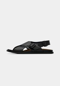 Μαύρα δερμάτινα σανδάλια με ανοιχτό σχεδιασμό και κοψίματα, ρυθμιζόμενους ιμάντες με αγκράφες και επίπεδη σόλα.