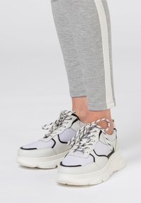 Chunkiga vita sneakers med grå nätpaneler, svarta accenter och tjocka sulor. Har mönstrade snören och en rundad tådesign.