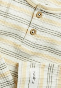 Tissu rayé et côtelé en crème, jaune et gris. Présente deux boutons beige et une petite étiquette avec le mot "newbie" sur le côté.