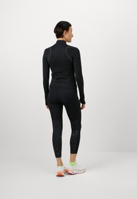 Sort langermet top og leggings med prikket mønster, tætsiddende design, fugttransporterende materiale, parret med hvide og orange løbesko.