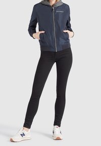 Marinfärgad bomberjacka med grå hoodie, dragkedja fram, sidofickor, ribbade ärmslut, bärs med svarta leggings och vita sneakers med blå detaljer.
